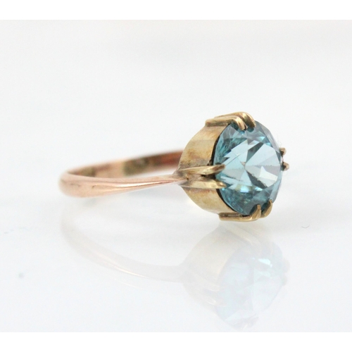 253 - An untested blue zircon dress ring, the round cut stone within double claw mount leading to plain po... 