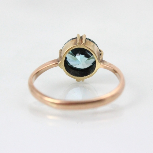 253 - An untested blue zircon dress ring, the round cut stone within double claw mount leading to plain po... 