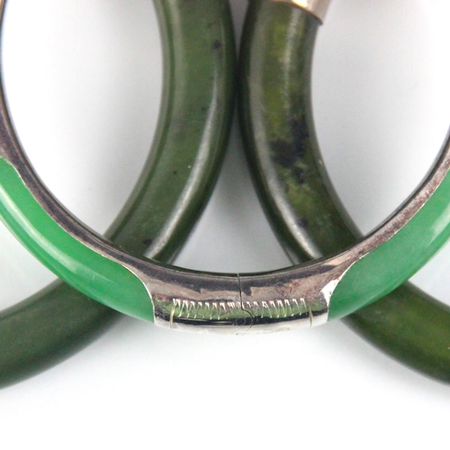 283 - A nephrite bangle, the plain polished bangle with white metal terminals engraved with floral detail,... 