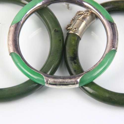 283 - A nephrite bangle, the plain polished bangle with white metal terminals engraved with floral detail,... 