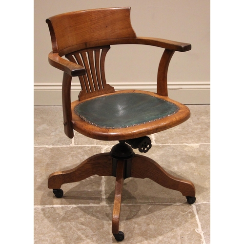 1033 - An oak revolving office desk chair, early 20th century, the curved arm rest and pierced central spla... 