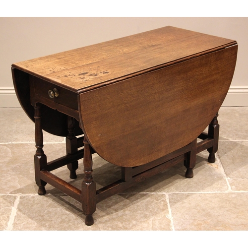 933 - A George III oak drop leaf dining table, the oval top above a single frieze drawer, upon ring turned... 