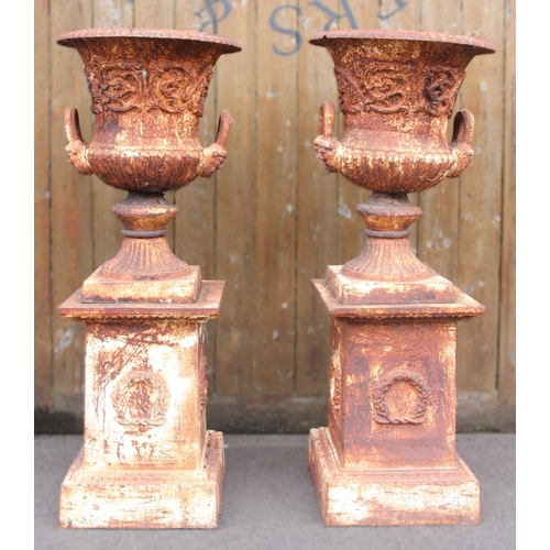 1109 - A pair of Victorian style cast iron urns on stands, the urns of campana form, each 62cm high, the re... 