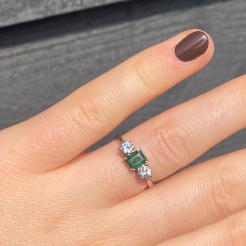 251 - An emerald and diamond three stone ring, the emerald cut stone with a round cut diamond to each side... 