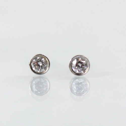 102 - A pair of diamond stud earrings, the round cut diamonds in 9ct white gold rubover mount, with post a... 