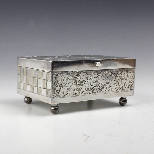 15 - An East African white metal jewellery box, the rectangular hinged cover with florally engraved decor... 