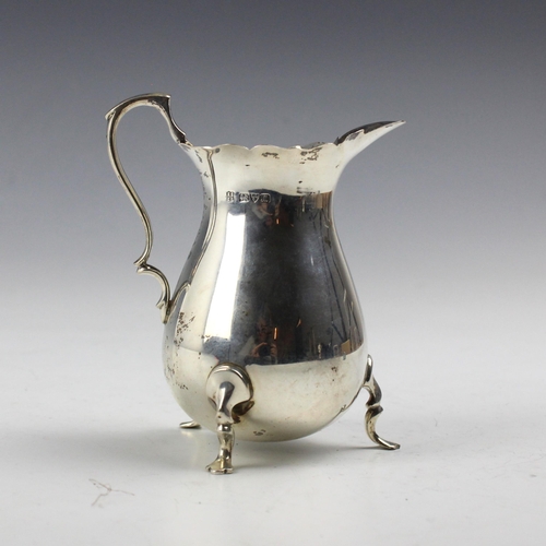 29 - A George V silver cream jug, Barker Brothers, Chester 1912, the shaped rim above a bulbous body, upo... 