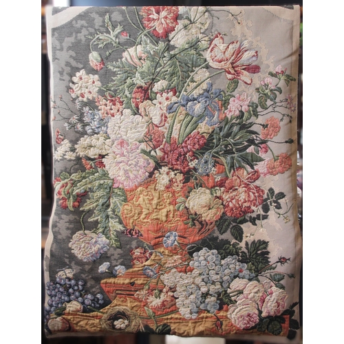 381 - A wall hanging tapestry, 20th century, machine woven, depicting a vase of blooms and fruit, upon an ... 