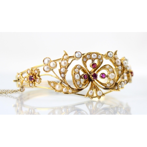 66 - A Victorian style untested ruby and pearl bangle, the central bow shaped motif set with four graduat... 