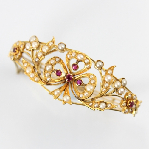 66 - A Victorian style untested ruby and pearl bangle, the central bow shaped motif set with four graduat... 