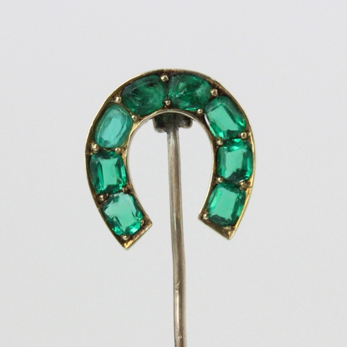 82 - An early 20th century green stone set stick pin, the horse shoe shaped head set with eight cushion c... 