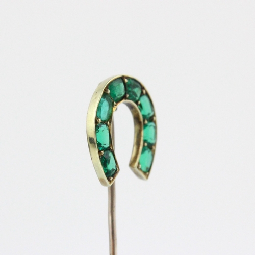 82 - An early 20th century green stone set stick pin, the horse shoe shaped head set with eight cushion c... 