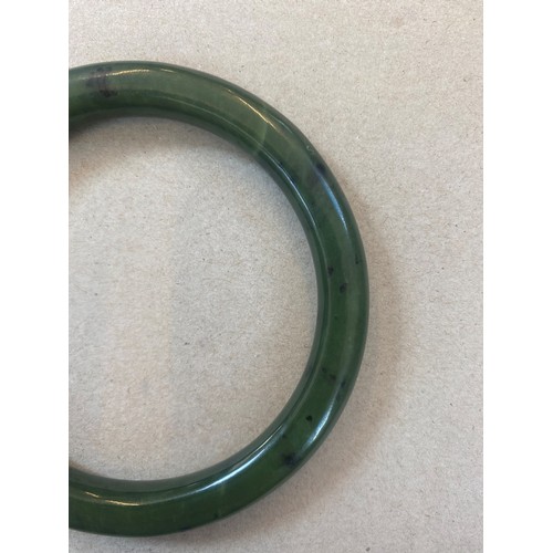 62 - A nephrite bangle, the plain polished bangle with white metal terminals engraved with floral detail,... 