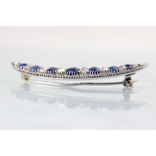 130 - An early 20th century diamond and untested sapphire crescent brooch, the seven graduated cushion cut... 