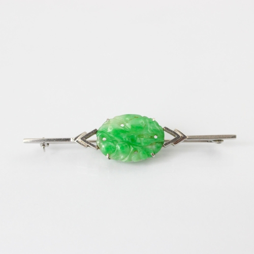 137 - An Art Deco jade brooch, the central oval carved panel depicting fruit and foliage, set in a white m... 