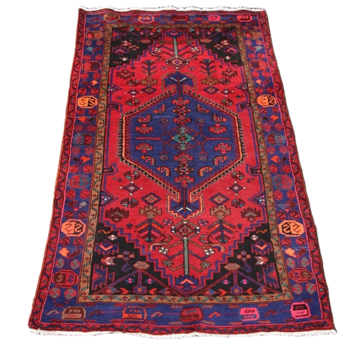 643 - A red ground Persian Hamadan village rug, with a central diamond medallion enclosed by spandrels and... 