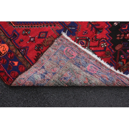 643 - A red ground Persian Hamadan village rug, with a central diamond medallion enclosed by spandrels and... 