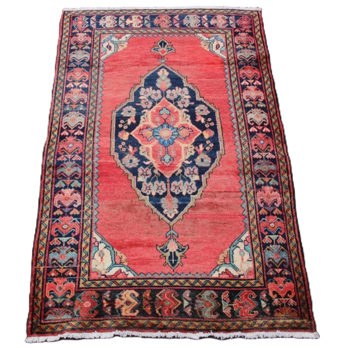 645 - A washed red ground Persian Surok village rug, with a large floral medallion design, 205cm x 122cm