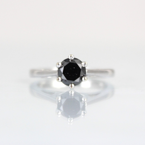 182 - A black diamond solitaire ring, the round cut diamond within white metal claw setting edge, leading ... 