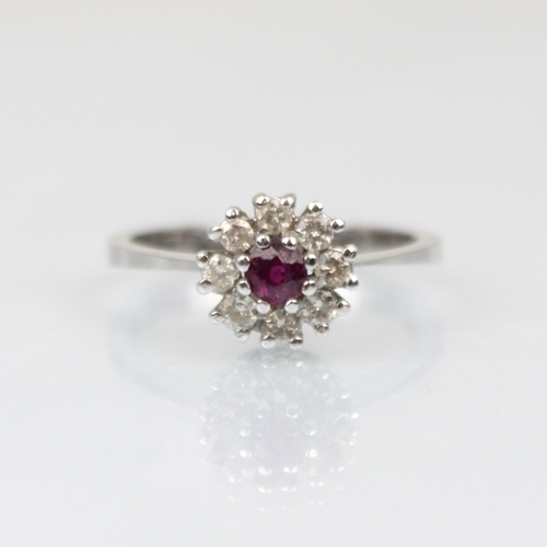 213 - A white metal diamond cluster ring, the central red stone within a surround of eight round cut diamo... 