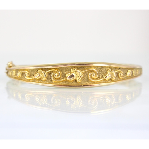 266 - A yellow metal bangle, the tapering florally engraved detail leading to plain polished re-verse, wit... 