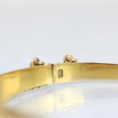 266 - A yellow metal bangle, the tapering florally engraved detail leading to plain polished re-verse, wit... 