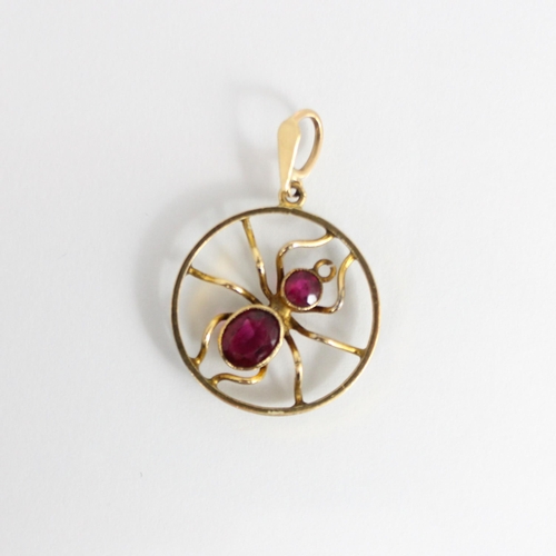 311 - A 20th century yellow metal pendant, the circular pendant encompassing a spider set with red stone b... 