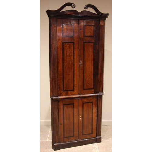 736 - A George III oak and mahogany cross banded freestanding corner cupboard, the swan neck pediment with... 