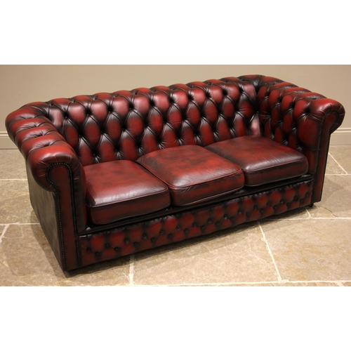 844 - An oxblood red leather Chesterfield sofa and conforming armchair, late 20th century, both of typical... 