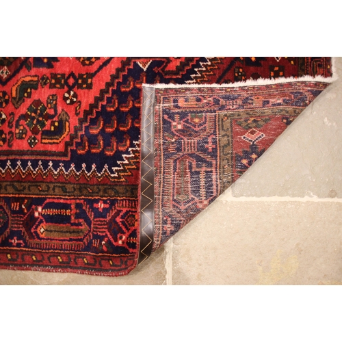 689 - A Caucasian hand knotted wool rug, in red, blue and green colourways, the central vibrant red lozeng... 