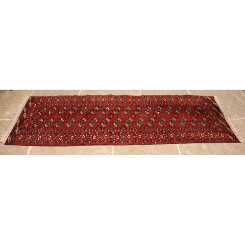 803 - A Bokhara wool runner, the central red field with traditional octagonal guls, enclosed by repeating ... 