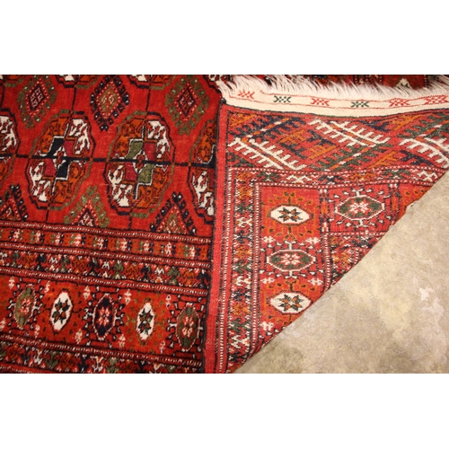 803 - A Bokhara wool runner, the central red field with traditional octagonal guls, enclosed by repeating ... 