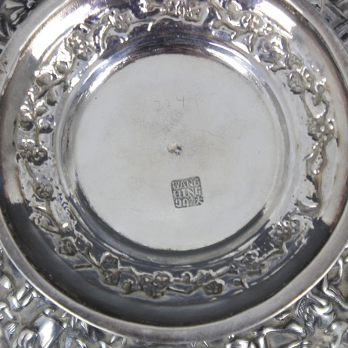 23 - A Chinese white metal comport, Wang Hing, the shaped rim above embossed bowl depicting figures among... 