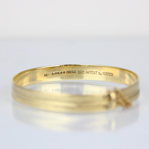 312 - A late 20th century 9ct yellow gold bangle, the bangle with engraved front, with slide mechanism, st... 