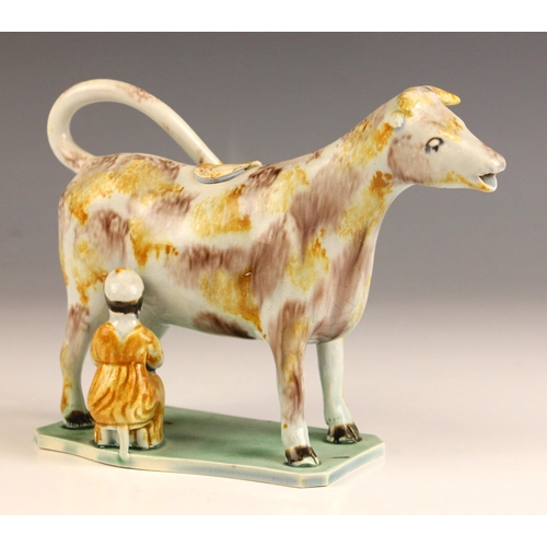 606 - An English pottery cow creamer and cover, circa 1810, on a wafer-thin base with maid, in a Pratt war... 