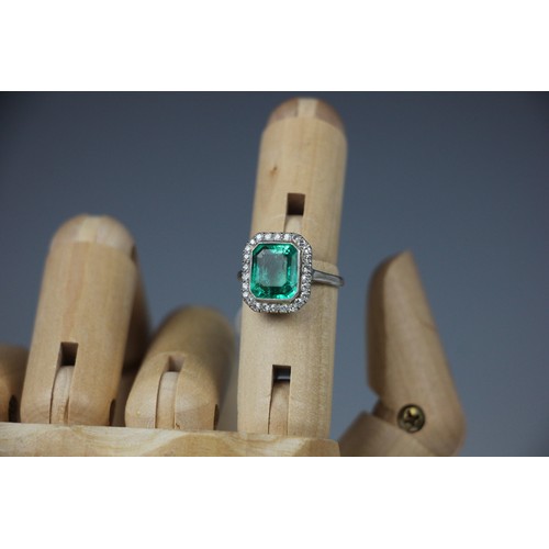 255 - An early 20th century untested emerald and diamond cluster ring, the central emerald cut emerald wit... 