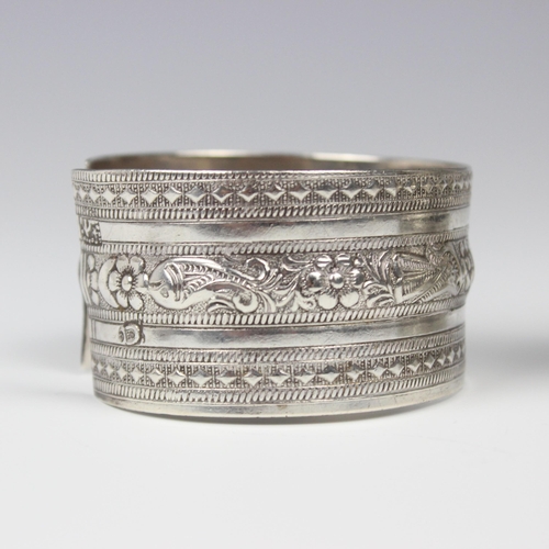 50 - A white metal Egyptian cuff, with repeating flowerhead and chevron engraved design, stamped to inter... 