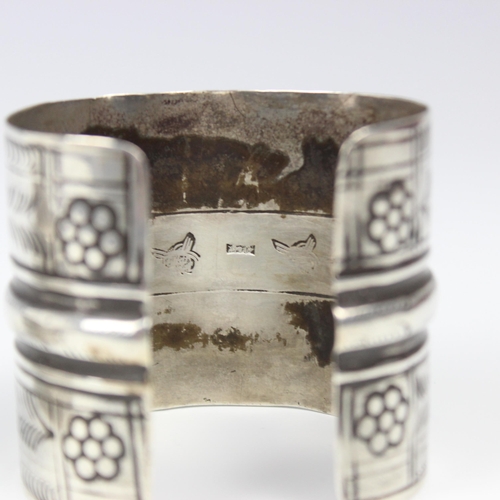 50 - A white metal Egyptian cuff, with repeating flowerhead and chevron engraved design, stamped to inter... 