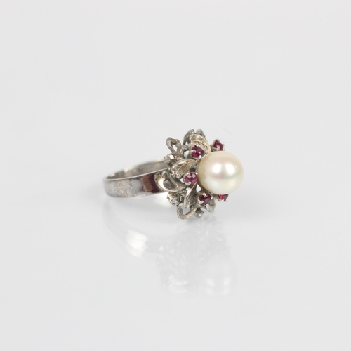 115 - A cultured pearl dress ring, the spherical pearl within stylised surround of red stones and white me... 