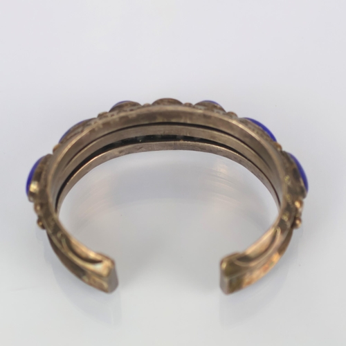 131 - A Navajo lapis lazuli cuff, the seven cabochon lapis lazuli within rub over setting leading to typic... 