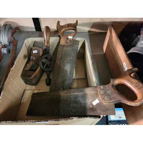 163 - A box containing two vintage hand saws, an old wooden plane and a hand drill