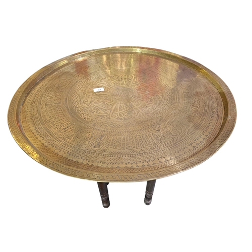 37 - Very large brass charger Indian influence on folding wooden turned legs 73cm in diameter