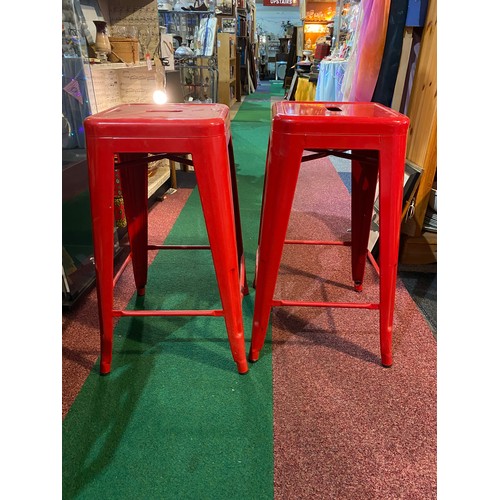 561 - 2 red metal stools, measuring 66 cm tall.