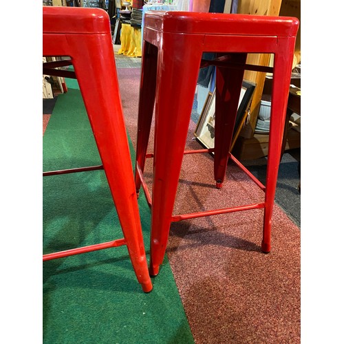 561 - 2 red metal stools, measuring 66 cm tall.