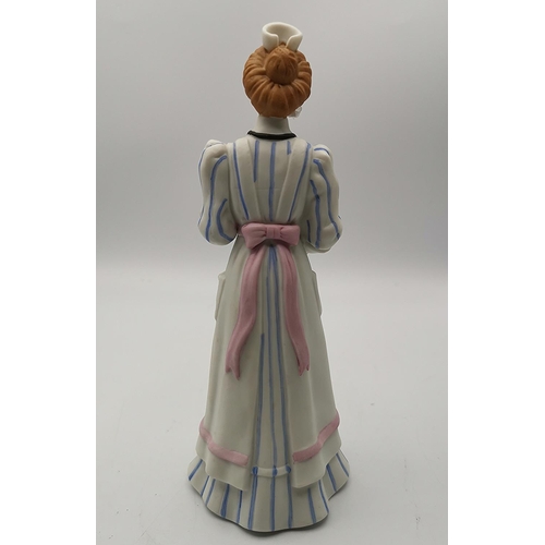 65 - ENESCO 19cm PORCELAIN CHARACTER FIGURINE OF A NURSE CARRYING A TEDDY BEAR.