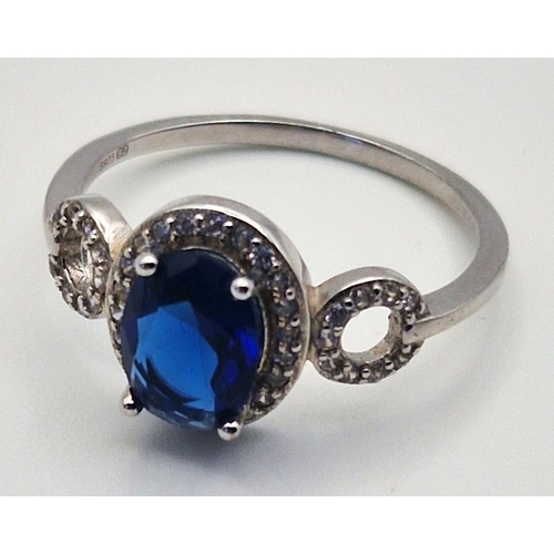 264 - SILVER (925) RING WITH OVAL CUT SIMULATED SAPPHIRE SURROUNDED BY SMALLER WHITE STONES (Size N-O , To... 