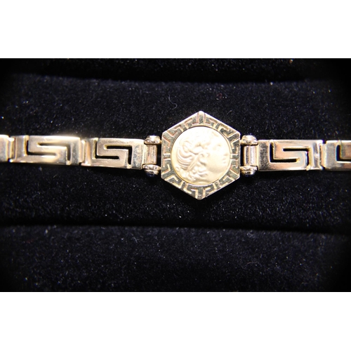 116 - A quality 18ct gold bracelet in a greek key design. With a 18ct gold coin pendant set with four smal... 