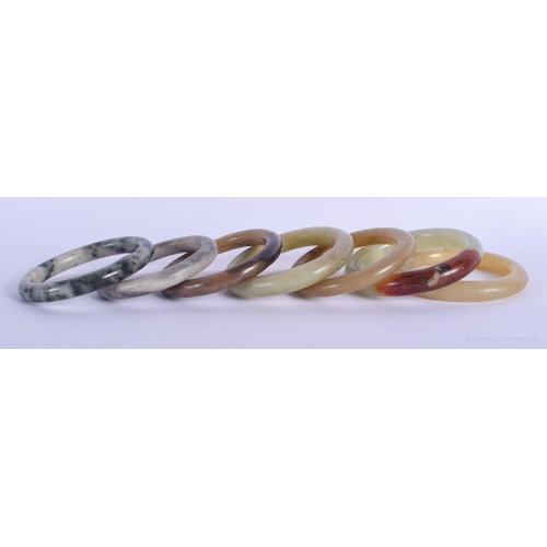 1154 - SEVEN CHINESE QING DYNASTY JADE & HARDSTONE BANGLES in various forms and sizes. 8.5 cm diameter. (7)