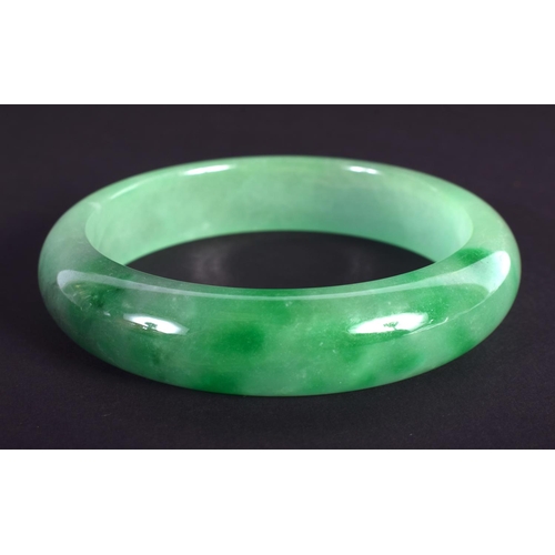 1264 - A CHINESE CARVED GREEN JADEITE BANGLE 20th Century. 7 cm diameter.