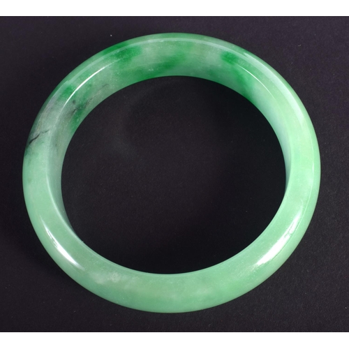 1264 - A CHINESE CARVED GREEN JADEITE BANGLE 20th Century. 7 cm diameter.